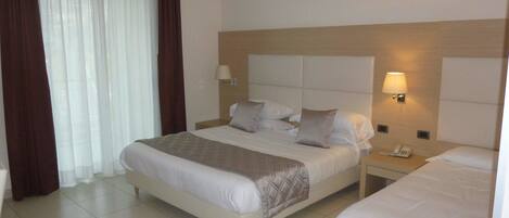 A hotel room with a large bed, a smaller bed, a nightstand with a phone, and a window with curtains.