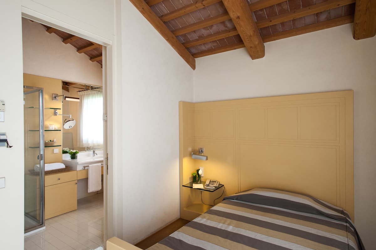 A bedroom with a bed, a bedside table with a lamp, and a bathroom with a shower and sink.