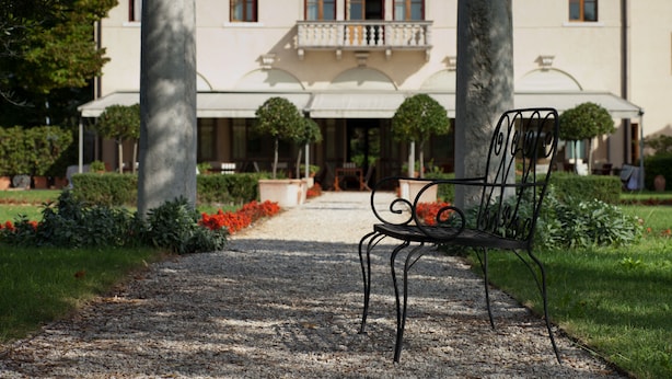 A pathway leading to a building with a balcony, surrounded by greenery and a bench. - Villa Ca' Sette (Bassano del Grappa)