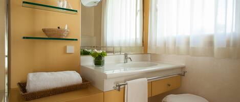 Un baño con un lavamanos blanco, un espejo, un perchero para toallas y un taburete pequeño.