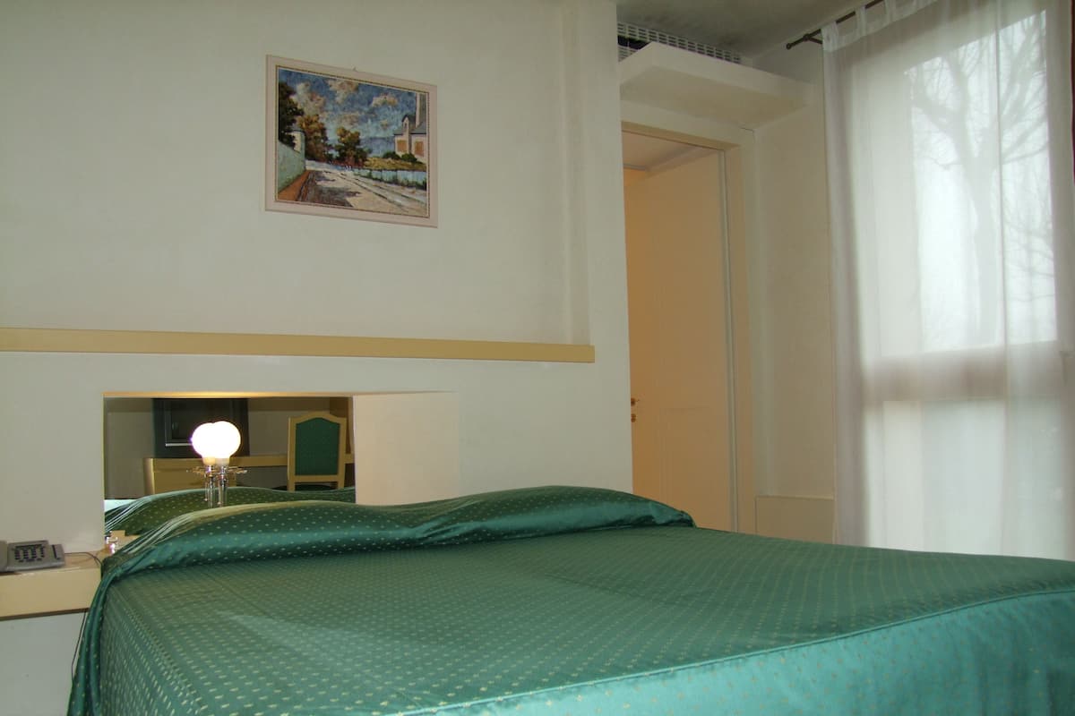 A hotel room with a bed, a bedside table, a mirror, and a painting on the wall.