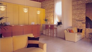A spacious living area with a stone wall, a yellow kitchen, and a white sofa with a black cushion. - Villa Ca' Sette (Bassano del Grappa)