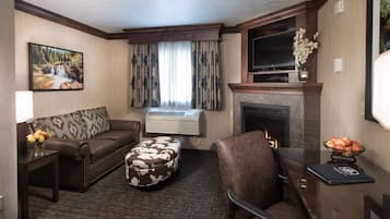Ein Hotelzimmer mit Sofa, Hocker, Sessel, Kamin, Fernseher und einem Bild von einem Wasserfall.
