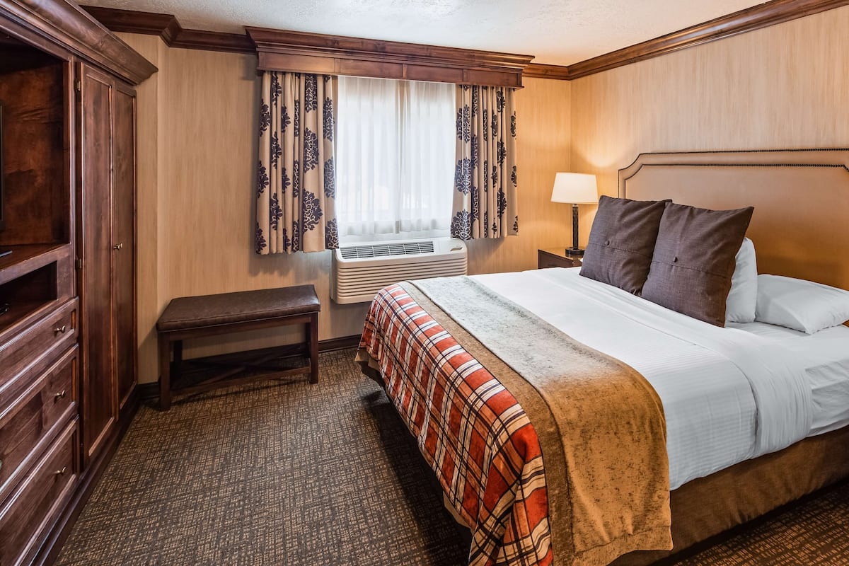 A hotel room with a bed, bedside lamps, a bench, a wardrobe, and a window with curtains.