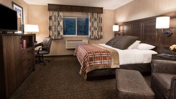 A hotel room with a bed, a desk, a chair, a TV, and a window with curtains.