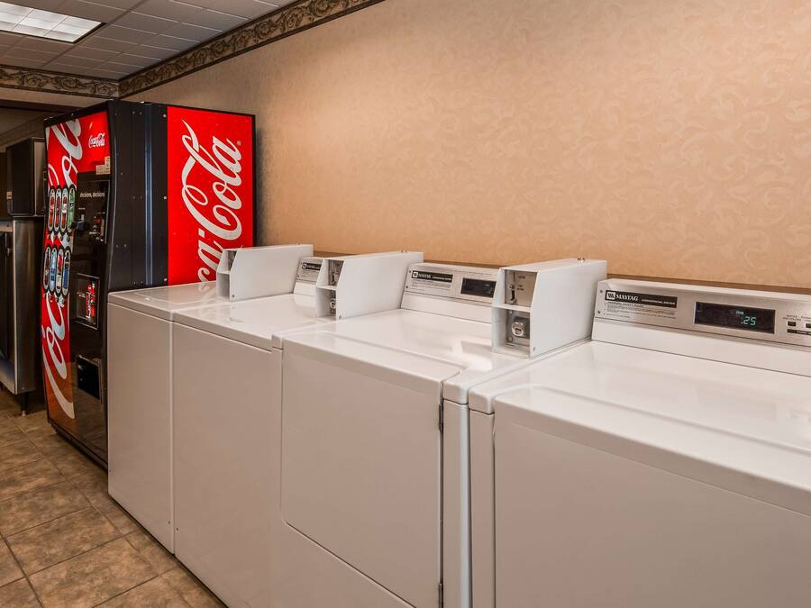 Ein Hotel-Waschraum mit vier weißen Waschmaschinen und Trocknern, einer Coca-Cola-Getränkeautomaten und einem Maytag-Trockner für den gewerblichen Gebrauch.