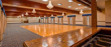 A spacious conference room with a wooden floor, multiple chandeliers, and a large sink area.