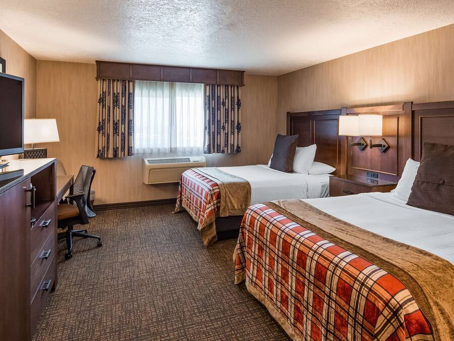 Habitación de hotel con dos camas, un escritorio con televisor, una silla, una ventana con cortinas y un equipo de aire acondicionado.