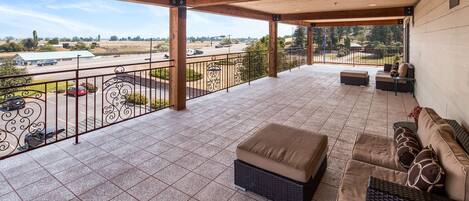 A covered outdoor patio with tiled flooring, a wrought iron railing, and a seating area with cushions.