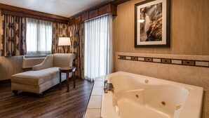 A hotel room with a sofa, a small table, a lamp, a bathtub, and a large framed picture on the wall. - Best Western Plus Flathead Lake Inn And Suites (Kalispell)