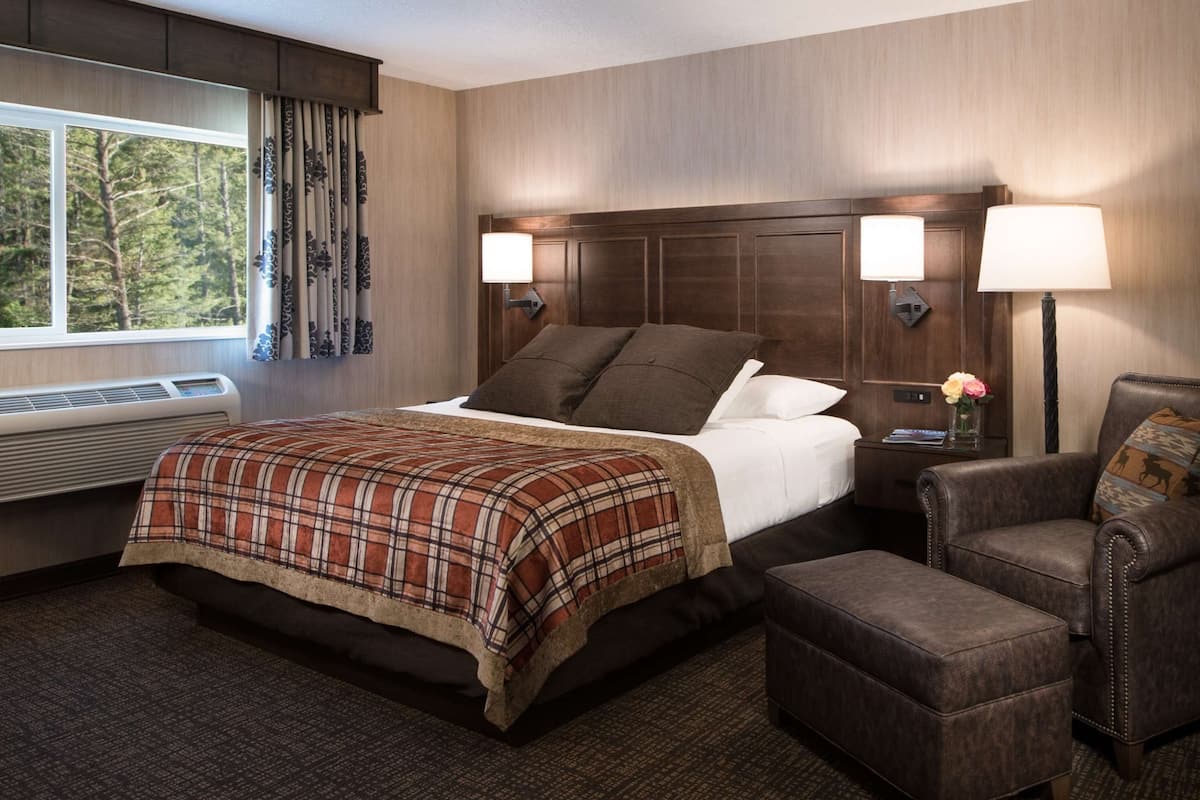 A hotel room with a bed, two bedside lamps, a chair, and a nightstand with a vase of flowers.
