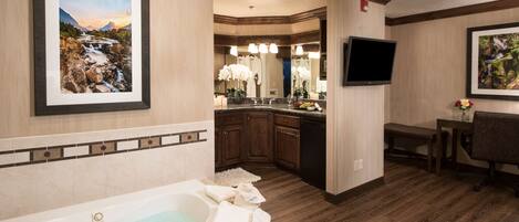 A hotel bathroom with a bathtub, a sink, a mirror, and a television.