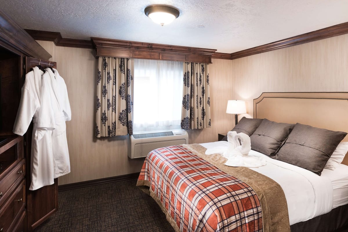 A hotel room with a bed, a bedside table with a lamp, a wardrobe, and a window with curtains.