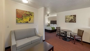 A hotel room with a gray sofa, a small table, a round dining table with chairs, a bed with white linens, and two wall-mounted paintings. - Best Western Mesquite Inn (Mesquite)
