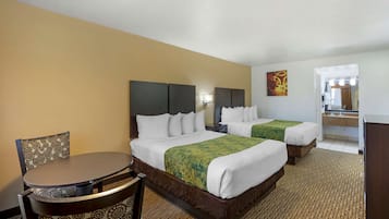 A hotel room with two beds, a round table, and a chair. There is a bathroom visible in the background.