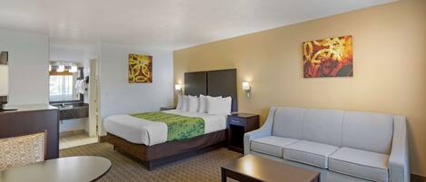 A hotel room with a bed, a sofa, a dining table, and a kitchenette.
