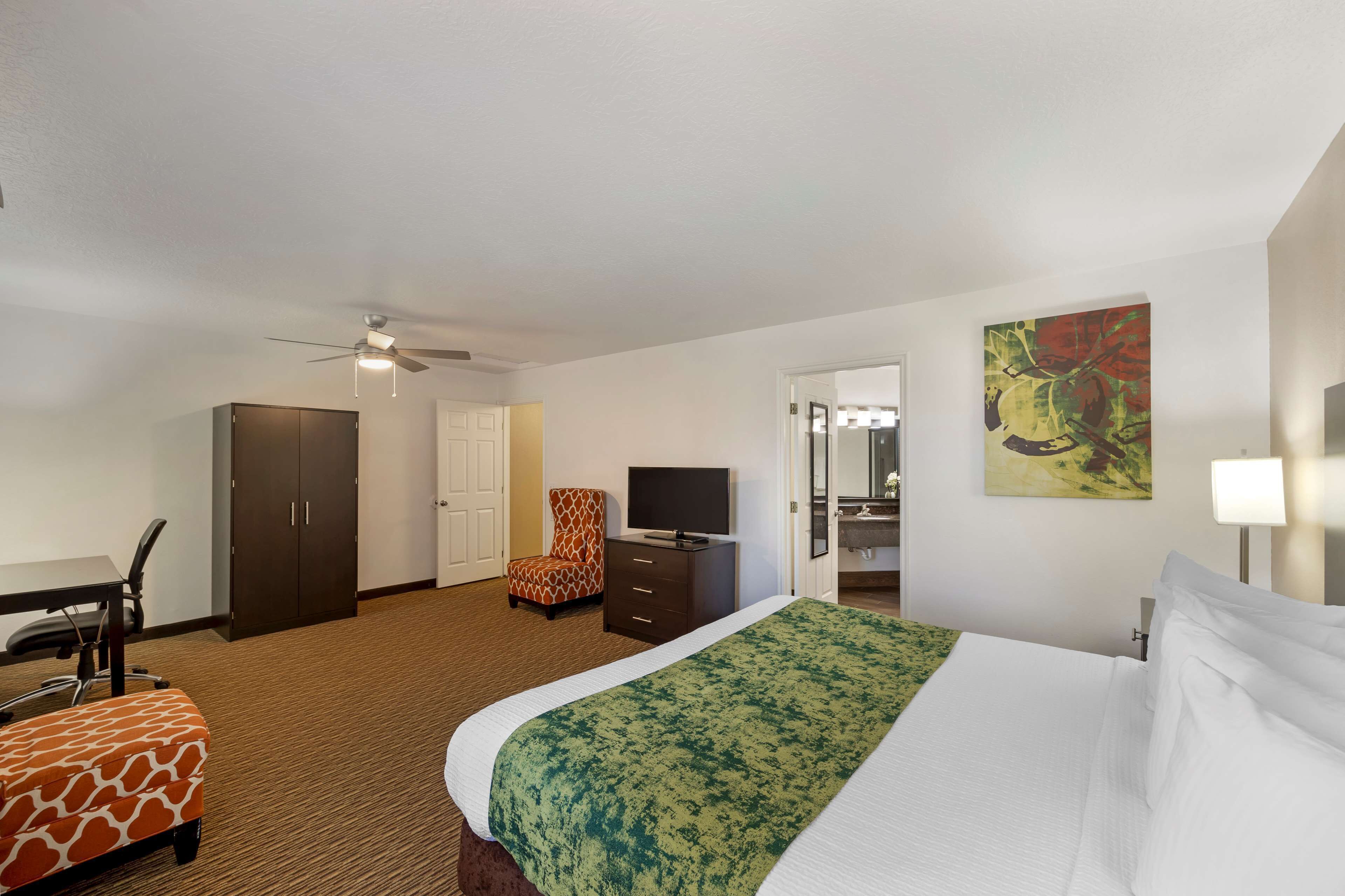 A hotel room with a bed, a desk, a chair, a wardrobe, a television, and a painting on the wall.