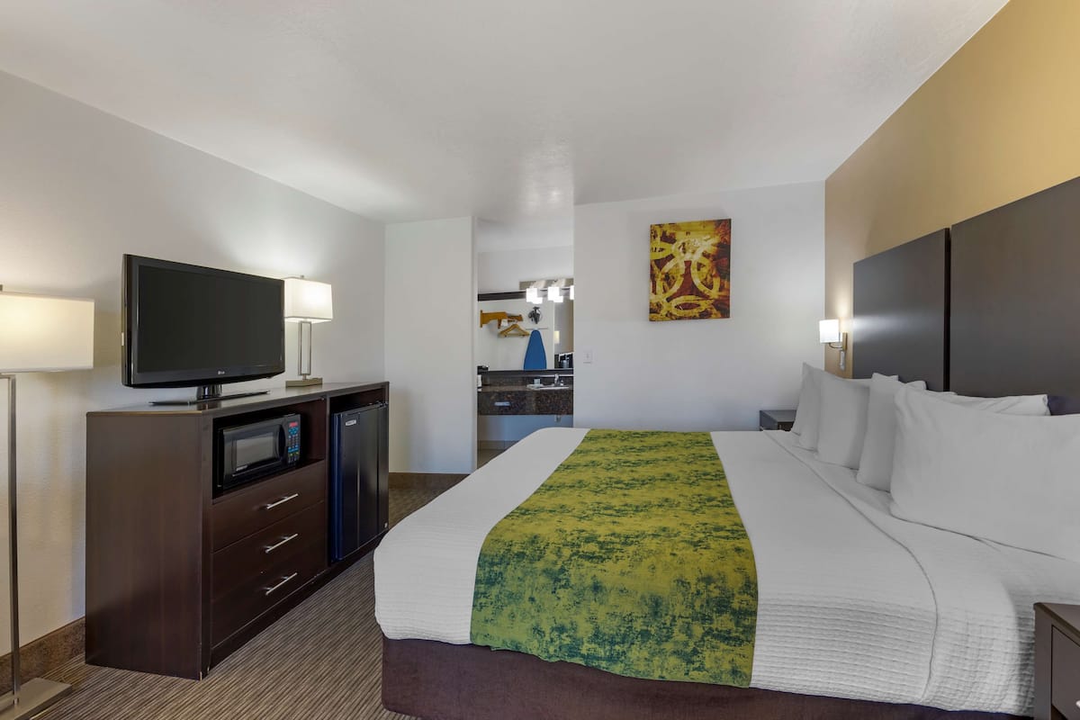 A hotel room with a large bed, a flat-screen TV, a microwave, a desk, and a vanity with a mirror.