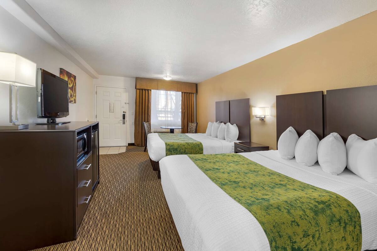 A hotel room with two beds, a desk with a television, and a window with curtains.
