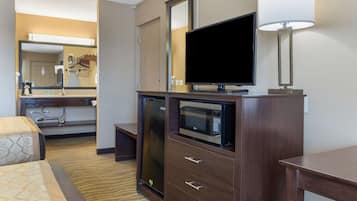 Een hotelkamer met een bed, een televisie, een magnetron, een koelkast, een bureau en een lamp.