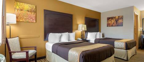 A hotel room with two beds, a chair, a desk, and a lamp.