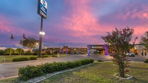 A Best Western hotel with a parking lot, flagpoles, and a landscaped area with a tree. - Best Western Taylor Inn (Taylor)