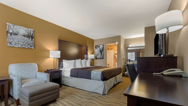 A hotel room with a bed, a chair, a desk, a lamp, and a painting on the wall. - Best Western Taylor Inn (Taylor)