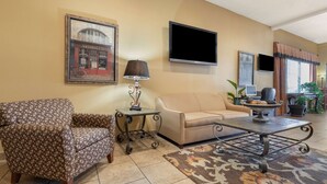 A living room with a patterned armchair, a beige sofa, a coffee table, and a television mounted on the wall. - Best Western Taylor Inn (Taylor)