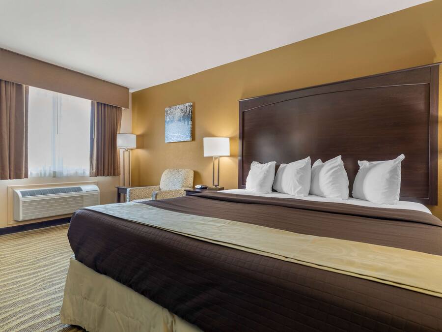 A hotel room with a large bed, a chair, a desk, a lamp, and a painting on the wall.