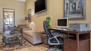 A hotel room with a sofa, a desk with a computer, a printer, a TV, a lamp, and a potted plant. - Best Western Taylor Inn (Taylor)