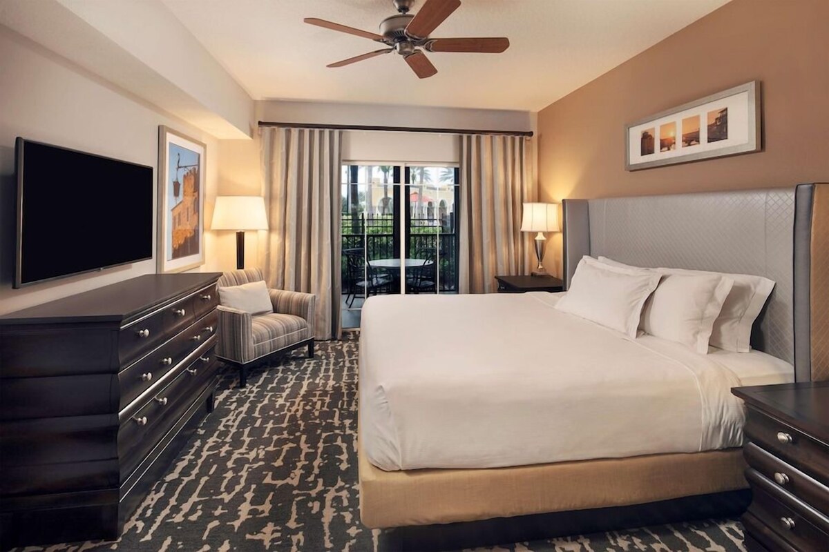 Une chambre d’hôtel avec un grand lit, une télévision à écran plat, un bureau, une chaise et un balcon avec vue.