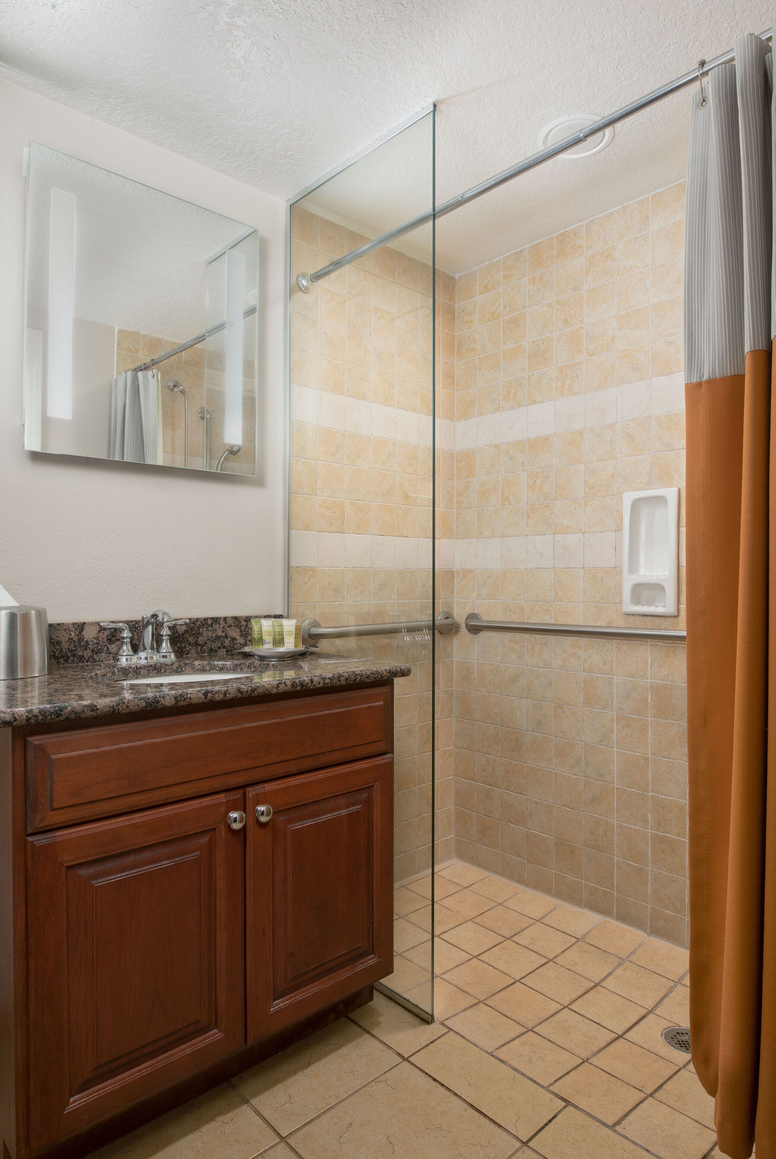 A bathroom with a glass shower enclosure, a wooden vanity, and a mirror.