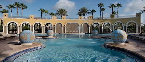 A pool with decorative spheres, palm trees, and a building with arches.