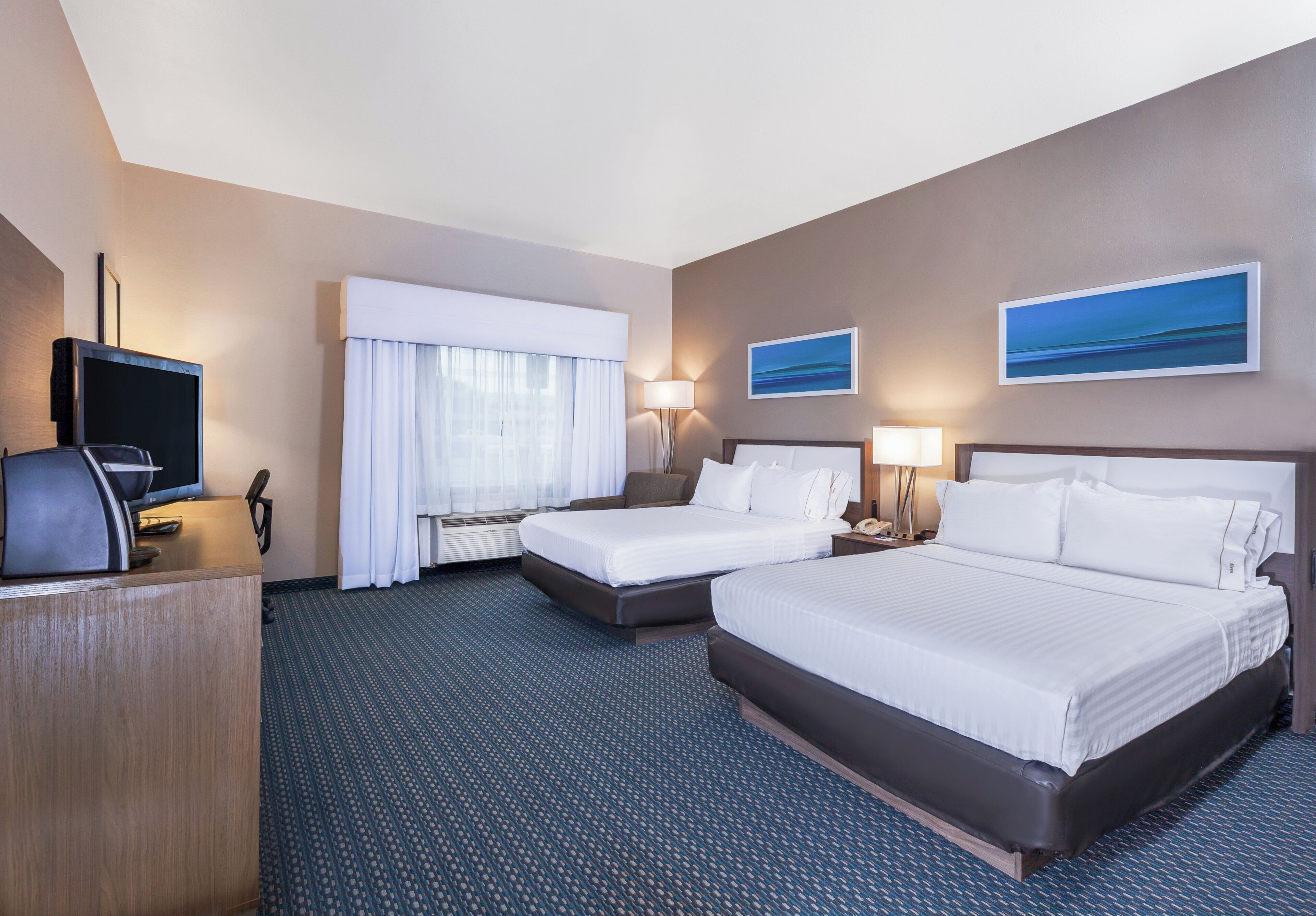 A hotel room with two beds, a desk with a television, and two bedside lamps.