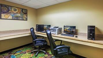 A hotel office with a desktop computer, printer, and two monitors. There are two chairs and a carpeted floor.