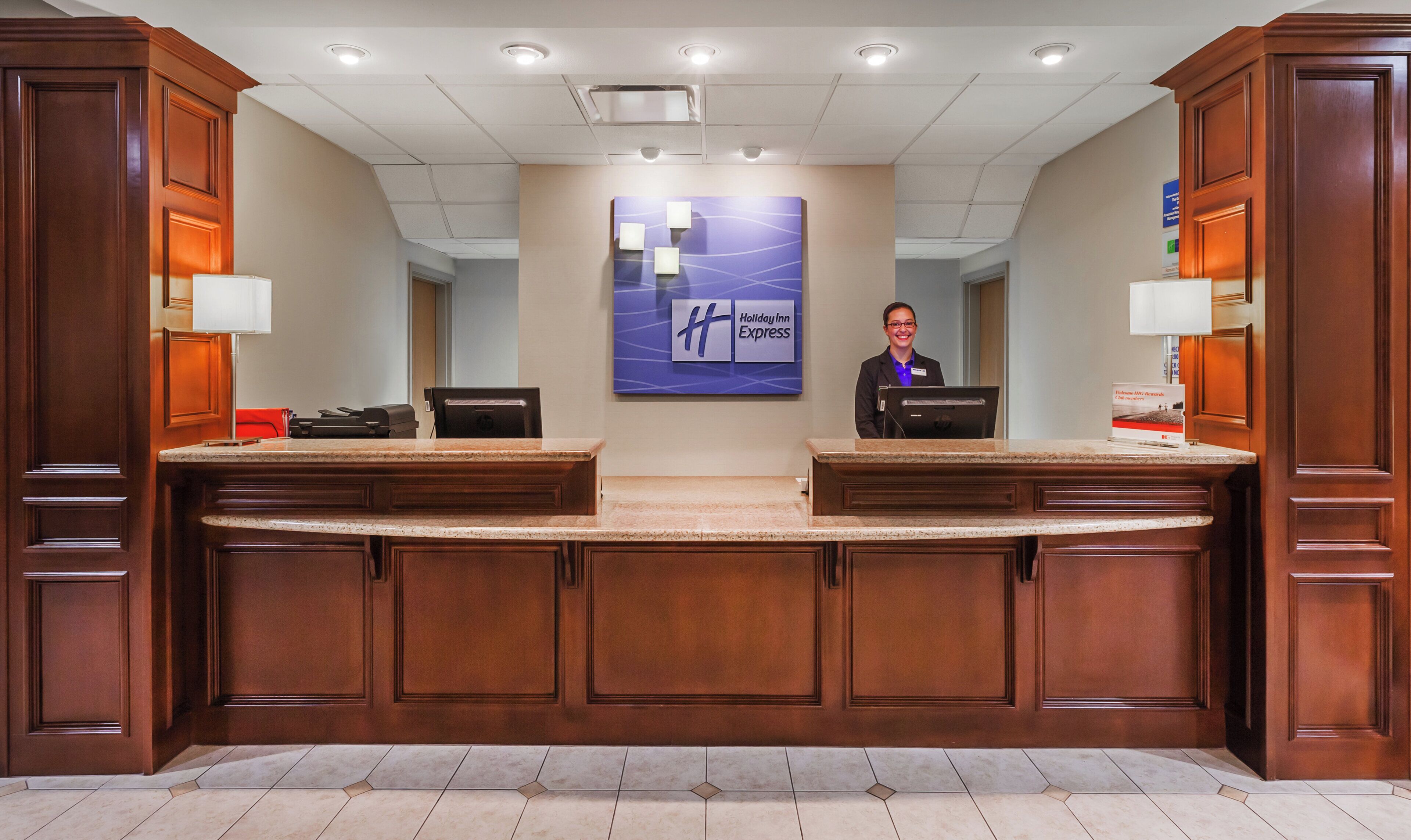 Balcão de recepção com a placa Holiday Inn Express, dois monitores de computador e uma etiqueta de identificação.