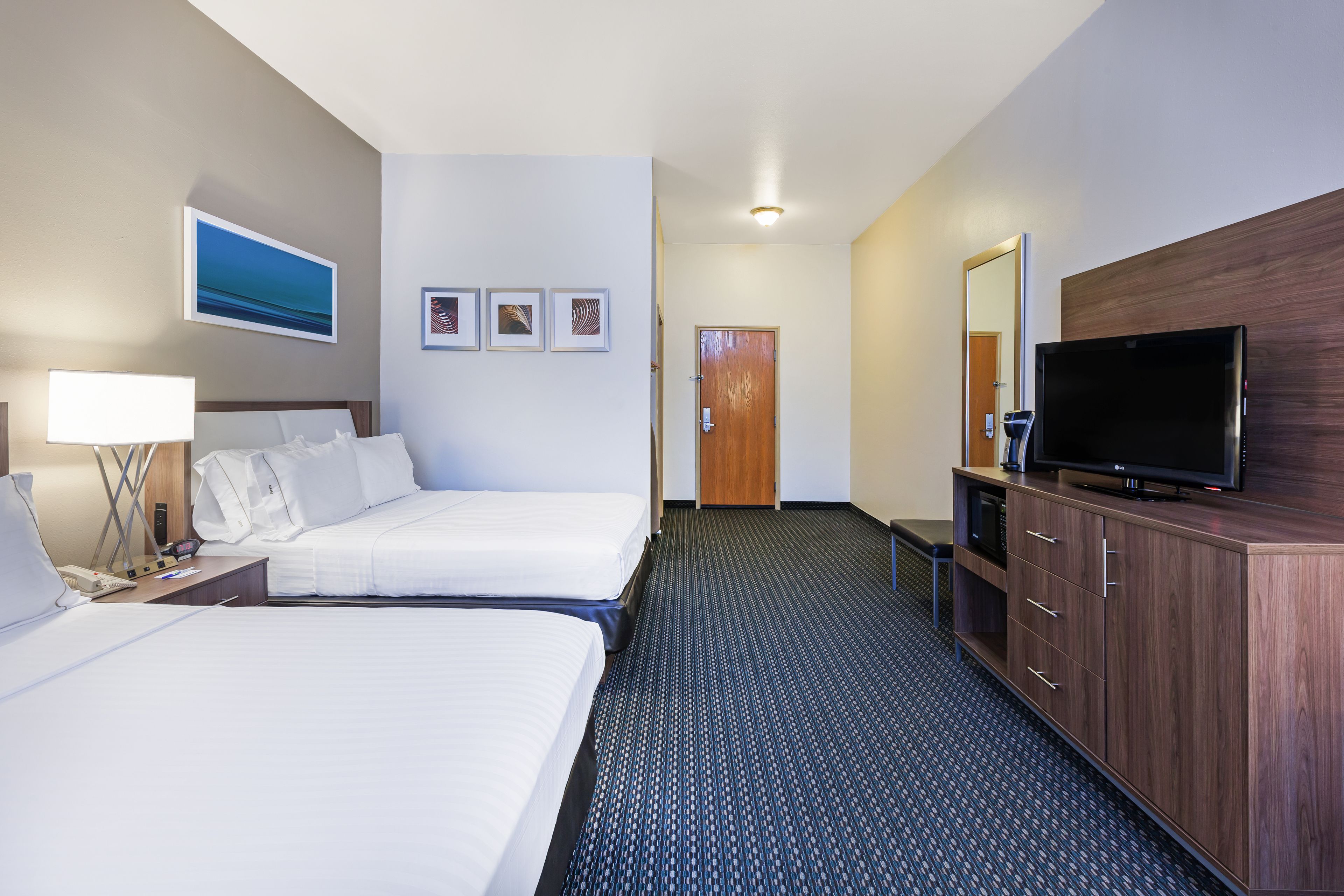 A hotel room with two beds, a TV, a desk with a lamp, and a carpeted floor.