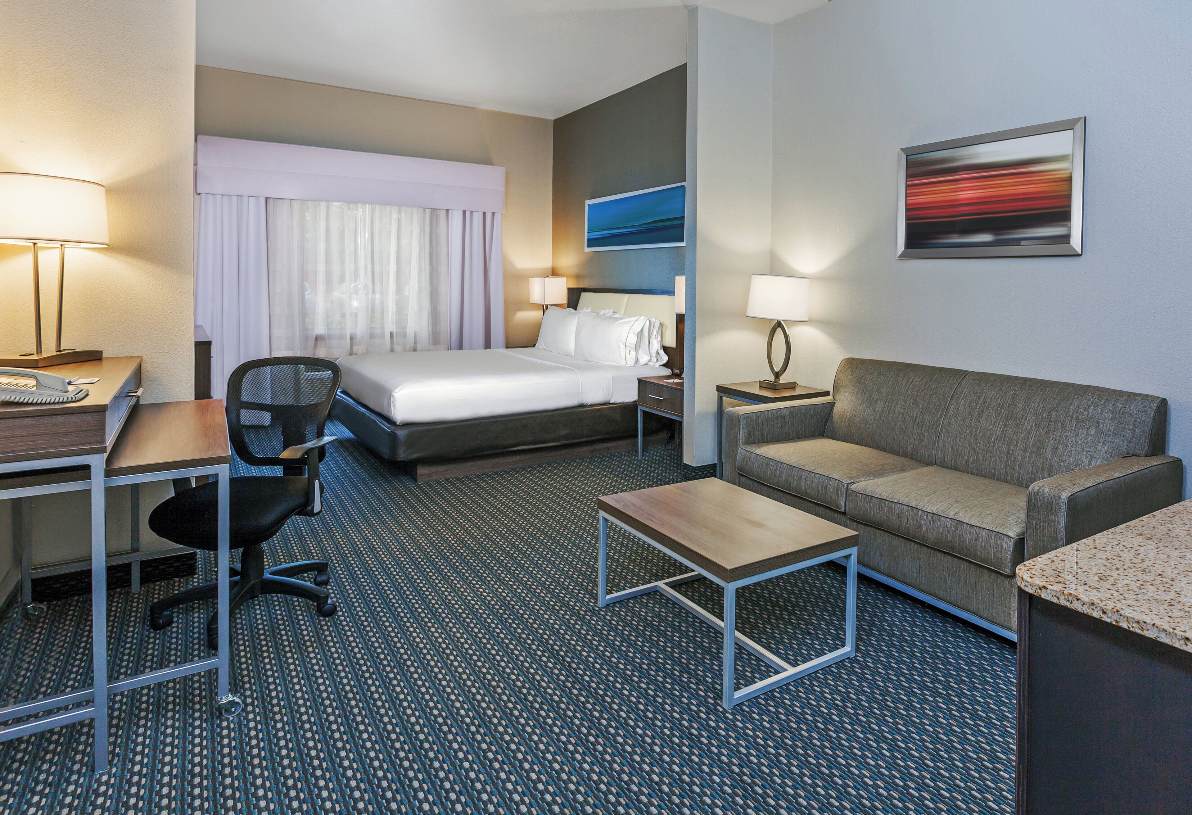 Habitación de hotel con cama, escritorio con teléfono, una silla, sofá, mesa de centro y un cuadro en la pared.