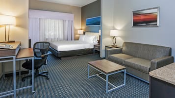 Habitación de hotel con cama, escritorio con teléfono, una silla, sofá, mesa de centro y un cuadro en la pared.