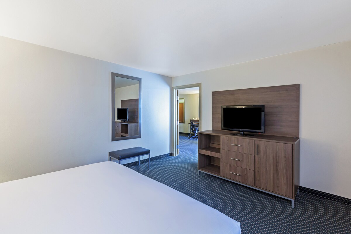 Ein Hotelzimmer mit einem Bett, einem Fernseher auf einer Holzkommode, einem Spiegel an der Wand und einer Tür zu einem weiteren Raum.