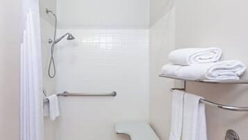 A shower area with a handheld showerhead, a grab bar, a bench, and a towel rack with folded towels.