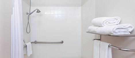 A shower area with a handheld showerhead, a grab bar, a bench, and a towel rack with folded towels.