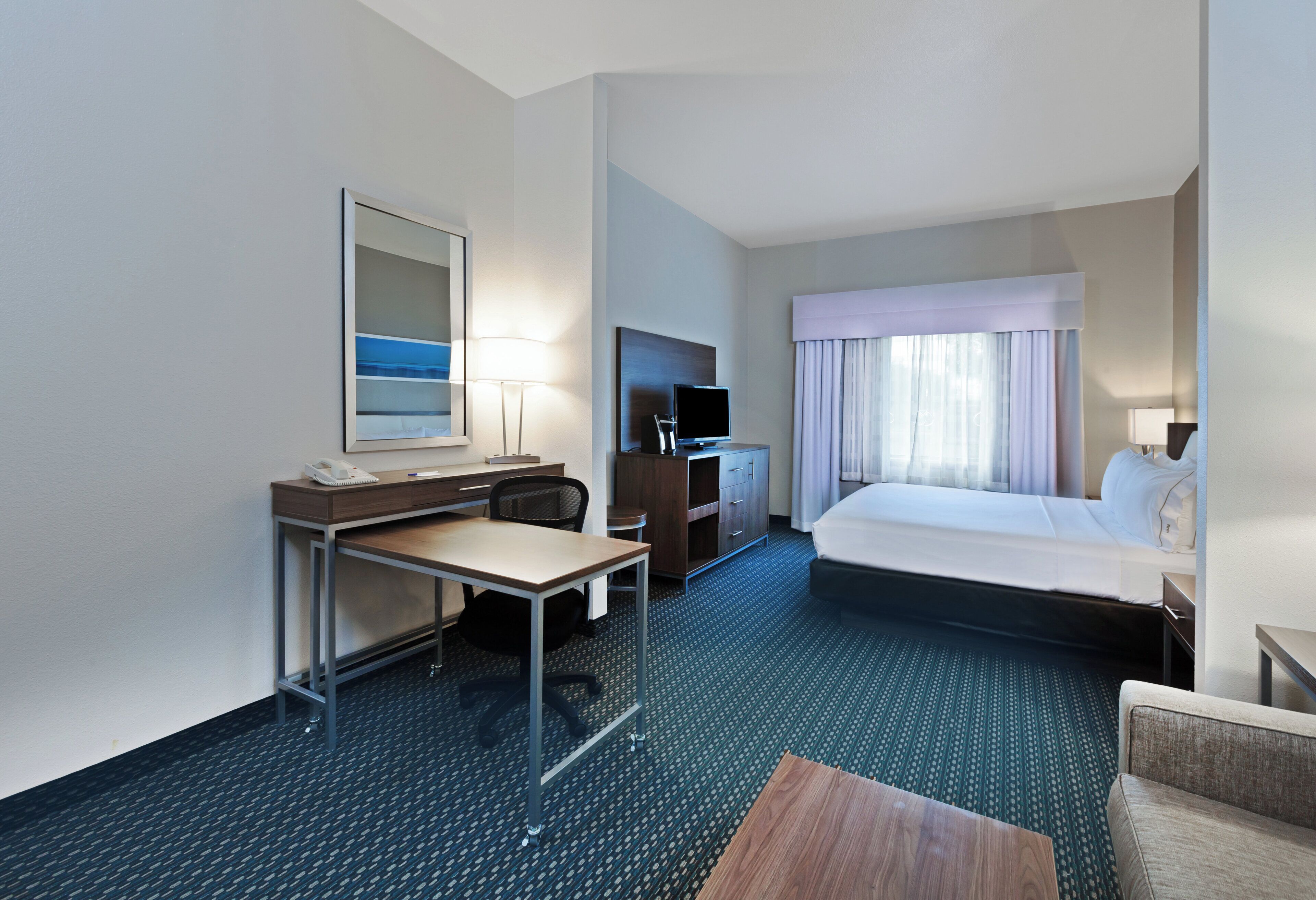 A hotel room with a bed, desk, chair, TV, and a window with curtains.