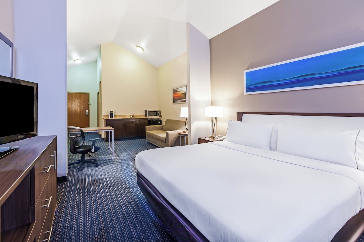 Ein Hotelzimmer mit Bett, Schreibtisch, Stuhl, Fernseher und einem Bild an der Wand.