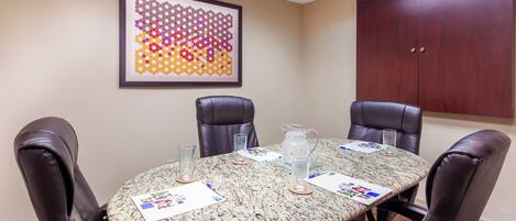 A conference room with a round table, four leather chairs, a framed abstract art piece, a wooden cabinet, and a water pitcher.