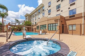 A hotel pool area with a hot tub, lounge chairs, and a building with multiple windows.