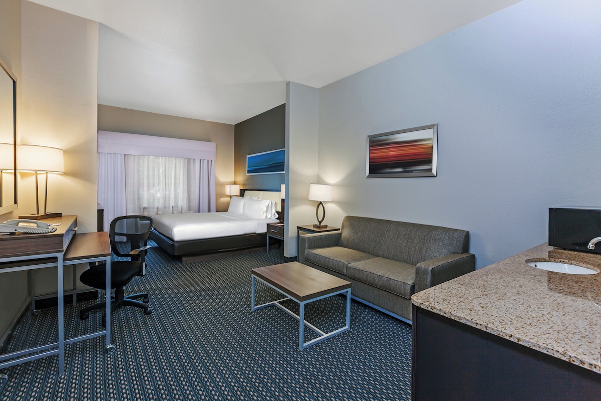 Ein Hotelzimmer mit Bett, Schreibtisch, Sessel, Schlafsofa und einem kleinen Tisch, sowie einem Badezimmer mit Waschbecken.