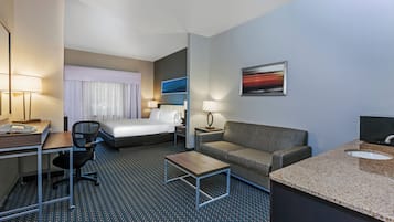 Habitación de hotel con cama, escritorio, silla, sofá, mesita y baño con lavamanos.
