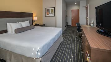 Ein Hotelzimmer mit einem großen Bett, einem Schreibtisch, einem Flachbildfernseher, einer Tür und einem gerahmten Bild an der Wand.