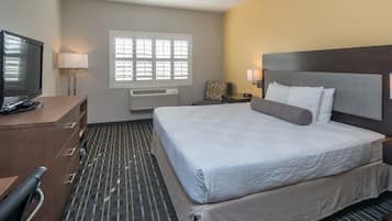 Habitación de hotel con una cama grande, un escritorio con televisor, una ventana con persianas y un calentador en la pared.